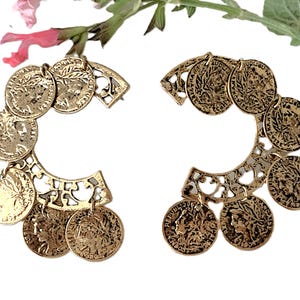 May include: A pair of gold-toned earrings with a coin design. Each earring features a circular design with multiple coins attached to a decorative metal frame.
