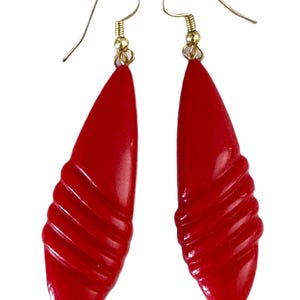 May include: A pair of red earrings with a teardrop shape. The earrings have a gold-colored hook and a textured, ridged design on the lower portion. The earrings are approximately 3 inches long.