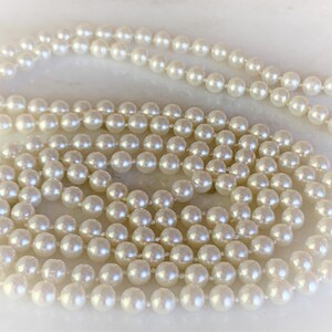 May include: A long strand of white pearls, arranged in a circular pattern on a white surface.