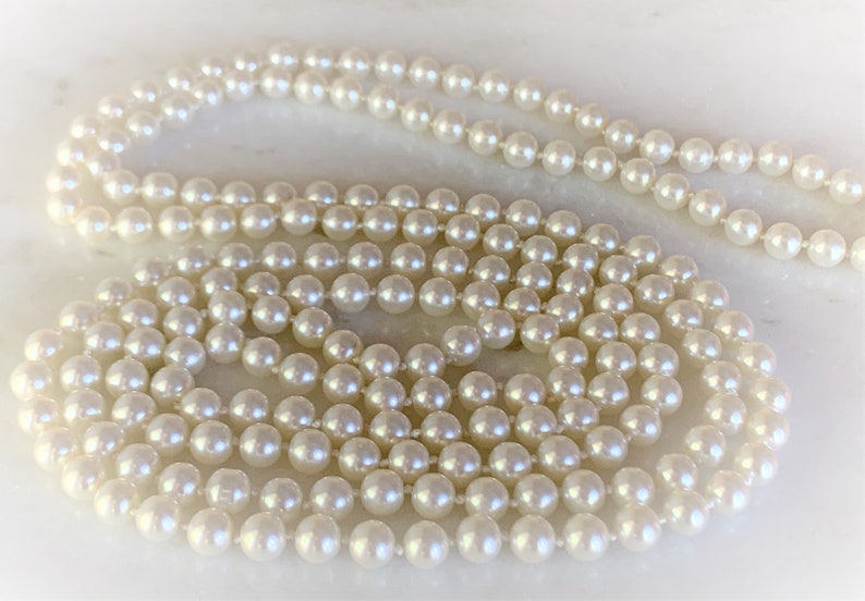 May include: A long strand of white pearls, arranged in a circular pattern on a white surface.