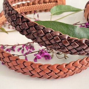 Peut inclure: Deux bandeaux en cuir tress&eacute;s, l'un brun et l'autre beige, sont pr&eacute;sent&eacute;s sur une surface blanche avec des fleurs violettes.
