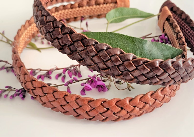Peut inclure: Deux bandeaux en cuir tress&eacute;s, l'un brun et l'autre beige, sont pr&eacute;sent&eacute;s sur une surface blanche avec des fleurs violettes.