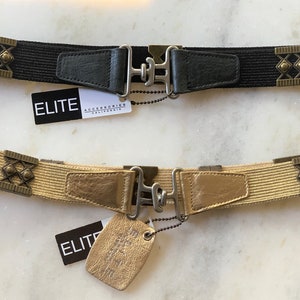 May include: Two elastic belts with metal hardware. One belt is black with a black leather tab and the other is tan with a gold leather tab. Both belts have decorative metal accents and a metal clasp.