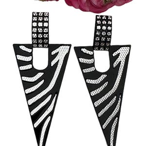 May include: A pair of triangular earrings featuring a matte black finish with silver-toned textured diagonal stripes. Each earring has a rectangular top post with a grid-like pattern of small silver studs, connecting to the main triangular body.