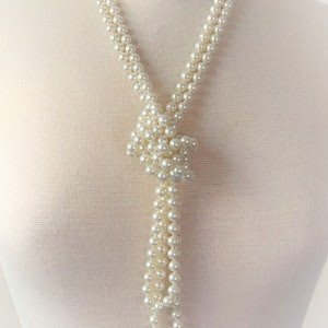 May include: A long white pearl necklace with a knotted design at the bottom. The necklace is on a white mannequin.