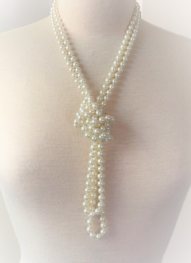 May include: A long white pearl necklace with a knotted design at the bottom. The necklace is on a white mannequin.