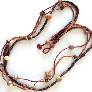 May include: A multi-strand necklace made of brown, orange, and gold wooden beads. The necklace is layered and has a tassel at the end.