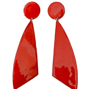 May include: A pair of bright red earrings. Each earring features a small, round stud connected to a larger, angular, triangular shape. The earrings have a glossy finish and are set against a white background.