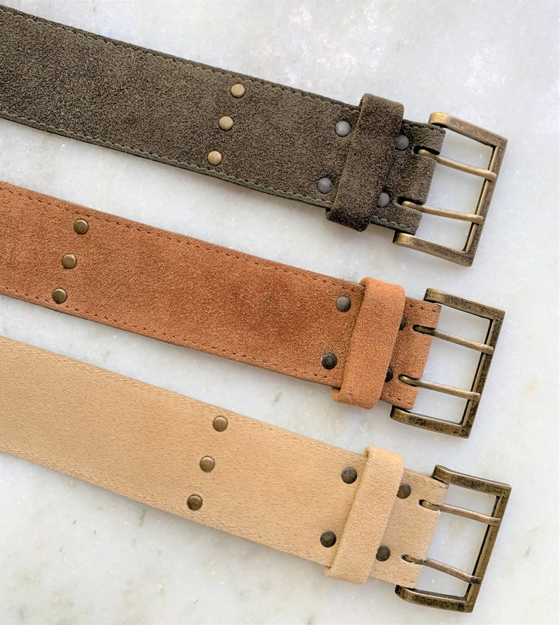 May include: Three suede belts with brass buckles. The belts are in different colors: brown, tan, and olive green.