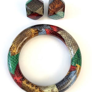 May include: A set of jewelry featuring a bangle bracelet and matching earrings. The bracelet and earrings have a patchwork design with various colors including red, green, brown, and gray. The earrings are geometric shaped with gold-colored hooks.