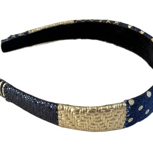 May include: A black headband with gold and blue patterned fabric. The headband has a woven gold fabric section and a blue fabric section with white polka dots.