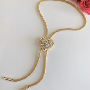 May include: A gold chain necklace with a heart-shaped pendant encrusted with clear rhinestones.