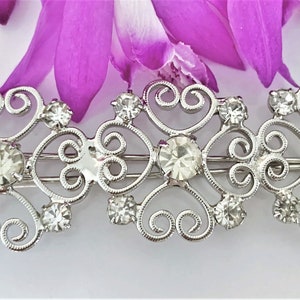 May include: Silver hair clip with a delicate, ornate design featuring swirls and clear rhinestones.