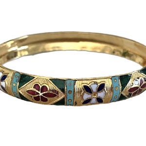 May include: A gold-toned bangle bracelet with intricate enamel detailing. The bracelet features a repeating pattern of floral designs in red, white, and blue, set against teal and green enamel sections. The overall design is ornate and decorative.