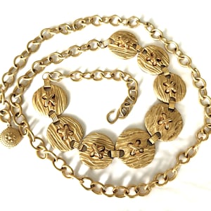 May include: A gold-tone chain belt with a series of large, round, textured, button-like links. The belt has a hook closure.