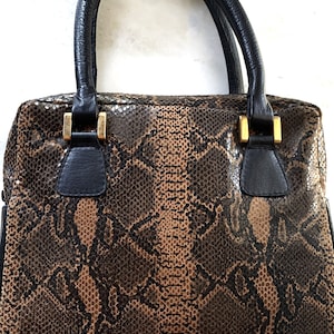 May include: A brown and black snakeskin handbag with black leather handles and gold accents.