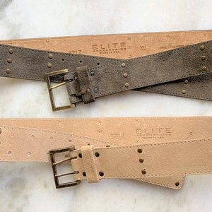 May include: Two suede belts with metal buckles and studs. The top belt is brown and the bottom belt is beige. Both belts have the text "ELITE ACCESSORIES MADE IN USA" printed on them.