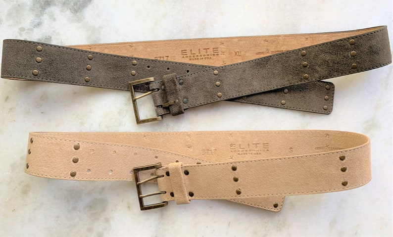 May include: Two suede belts with metal buckles and studs. The top belt is brown and the bottom belt is beige. Both belts have the text "ELITE ACCESSORIES MADE IN USA" printed on them.
