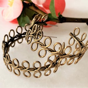 May include: A pair of gold-toned hoop earrings with a delicate, intricate design. The earrings are made of wire that is twisted and looped to create a floral pattern.