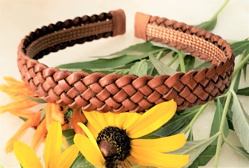 Peut inclure: Un serre-t&ecirc;te en cuir marron avec un motif tress&eacute;. Le serre-t&ecirc;te est sur une surface blanche avec des fleurs jaunes.