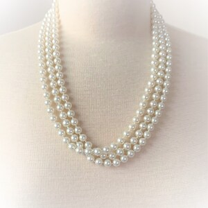May include: A three-strand pearl necklace made of white faux pearls. The necklace is on a white mannequin bust.