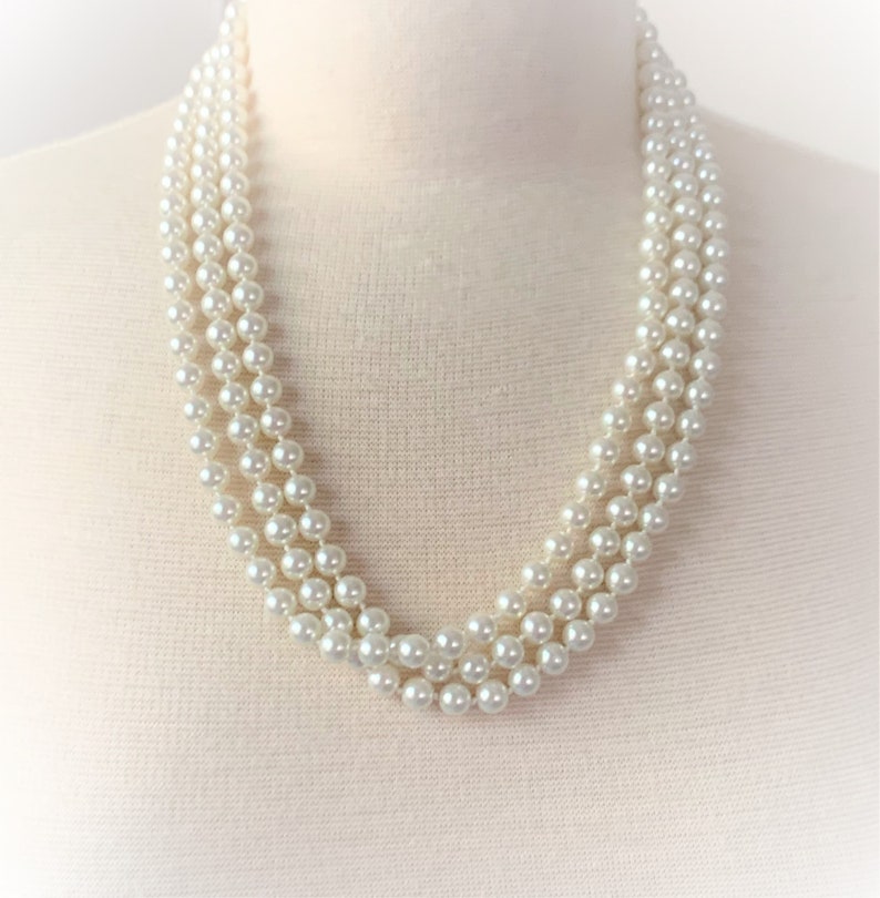 May include: A three-strand pearl necklace made of white faux pearls. The necklace is on a white mannequin bust.