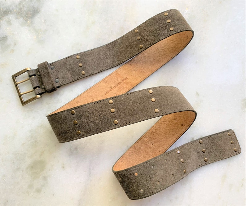 May include: A brown suede belt with gold-toned metal studs and a buckle. The belt is folded in a loop.