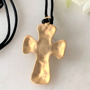 May include: A gold-toned cross pendant with a textured surface, hanging from a black cord necklace.