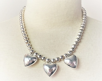 May include: A silver necklace with a beaded chain and three silver heart charms.