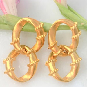 May include: A pair of gold-toned earrings with a double-loop design. The loops are twisted and have a rope-like texture.