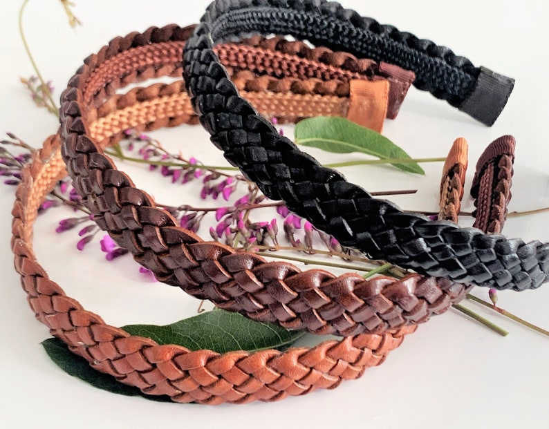 Peut inclure: Trois bandeaux en cuir tress&eacute; en marron, beige et noir. Les bandeaux sont empil&eacute;s les uns sur les autres et reposent sur une surface blanche avec des fleurs violettes.