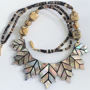 May include: A multi-strand necklace with brown and white beads and a large pendant made of iridescent mother-of-pearl tiles in a leaf shape.
