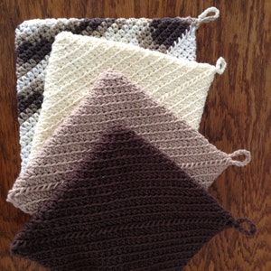 May include: Four crocheted pot holders in various shades of brown, beige, and white. The pot holders are stacked on top of each other, with the darkest brown pot holder on the bottom and the lightest beige pot holder on top.