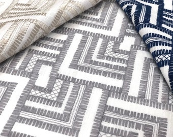 May include: Close-up of three fabric swatches with geometric patterns. The top swatch is a light beige with a silver thread design. The middle swatch is white with a gray geometric pattern. The bottom swatch is white with a navy blue geometric pattern.