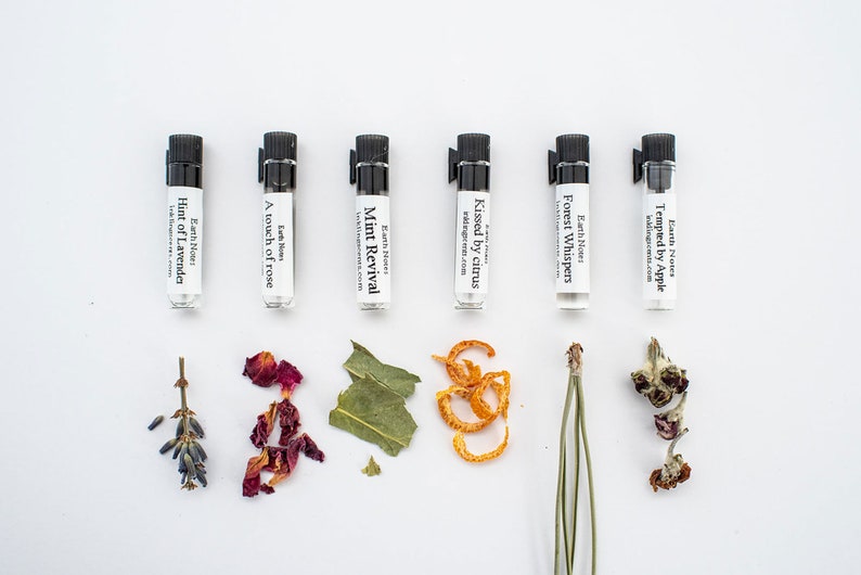 Puede incluir: Seis peque&ntilde;os frascos de vidrio con tapas negras y etiquetas que contienen diferentes aceites esenciales. Las etiquetas tienen los nombres de las fragancias: "Hint of Lavender", "A touch of rose", "Mint Revival", "Kissed by citrus", "Forest Whispers" y "Tempted by Apple". Flores y hierbas secas est&aacute;n dispuestas frente a cada frasco.