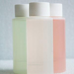 以下が含まれることがあります： 白いキャップが付いた透明なプラスチック製の小さなボトルが3本。ボトルには、緑、透明、ピンクの異なる色の液体が入っています。