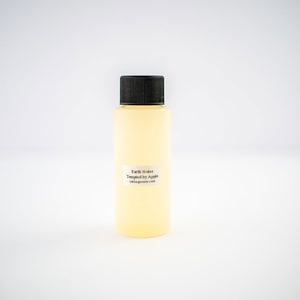 May include: A clear glass bottle with a black cap filled with a light yellow liquid. The bottle has a white label with the text "Earth Notes Tempted by Apple  bakingredients.com".