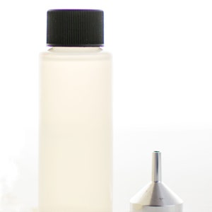 以下が含まれることがあります： 黒いキャップと小さな金属製のじょうごが付いた透明なプラスチックボトル。ボトルは円筒形で不透明で、黒いリブ付きキャップが付いています。じょうごは銀色で円錐形です。