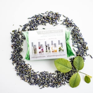 Puede incluir: Un conjunto de cinco peque&ntilde;os frascos de vidrio con diferentes l&iacute;quidos de colores y flores secas en su interior. Los frascos est&aacute;n etiquetados con "Earth Notes" y tienen el sitio web "inklingscents.com" impreso en la etiqueta. Los frascos est&aacute;n rodeados de flores de lavanda secas y hojas verdes.