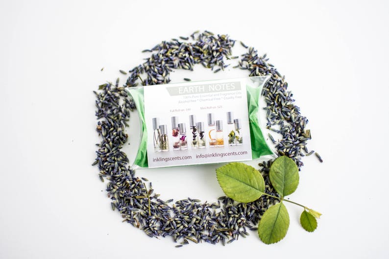 Puede incluir: Un conjunto de cinco peque&ntilde;os frascos de vidrio con diferentes l&iacute;quidos de colores y flores secas en su interior. Los frascos est&aacute;n etiquetados con "Earth Notes" y tienen el sitio web "inklingscents.com" impreso en la etiqueta. Los frascos est&aacute;n rodeados de flores de lavanda secas y hojas verdes.