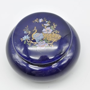 May include: A cobalt blue ceramic trinket box with a lid featuring a gold and blue peacock design with floral accents.