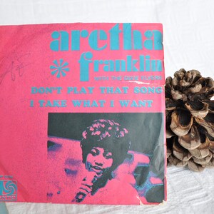 Può includere: Un disco in vinile da 45 giri rosa e blu con una foto di Aretha Franklin sul lato anteriore. Il disco è intitolato "Don't Play That Song (I'll Take What I Want)" e presenta il testo "With The Dixie Flyers".