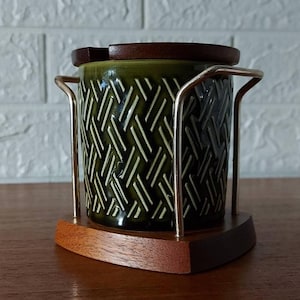 May include: A vintage green ceramic utensil holder with a woven pattern, set in a wooden base and frame. The holder has a dark wooden lid and a gold-coloured metal frame. The design is mid-century modern.