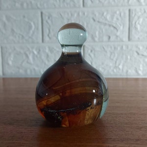 May include: A brown glass paperweight with a clear glass top. The paperweight has swirls of brown, orange, and white glass.