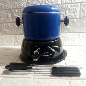 May include: A blue fondue pot with a black base and a set of fondue forks. The pot has a lid and two black handles. The forks have black handles with coloured tips.