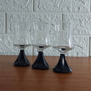 May include: Three clear glass shot glasses with black stems. The glasses have a flared bowl and a wide base.