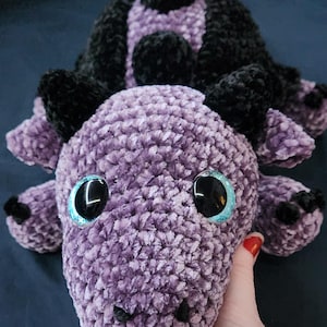May include: A purple and black crocheted dragon plush toy with large blue eyes.