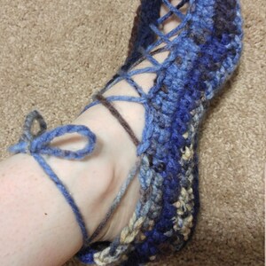 May include: Blue, brown, and beige crocheted slipper with a lace-up design. The slipper is tied at the ankle with a blue ribbon.