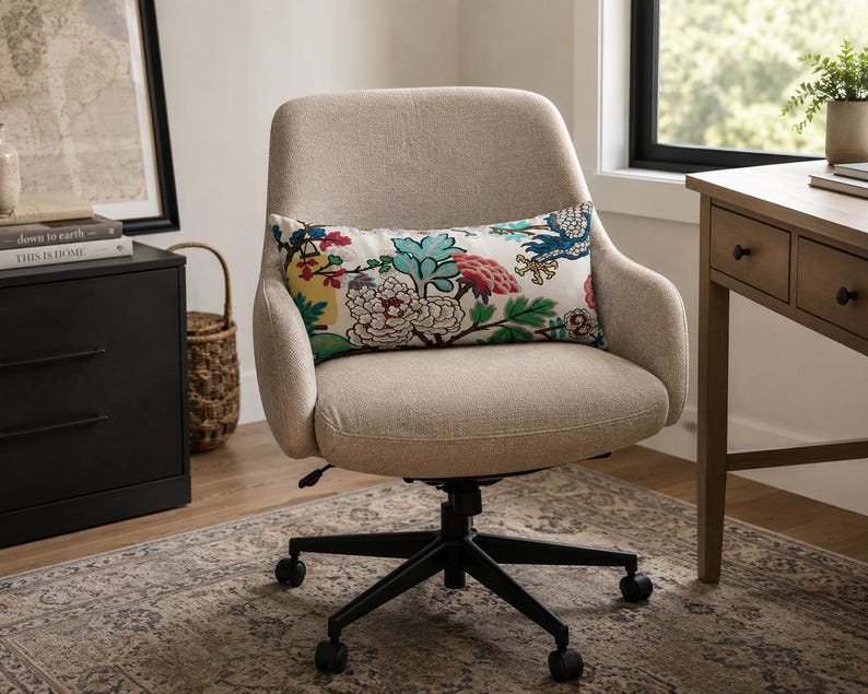 May include: A beige upholstered office chair with a black five-point base on casters. A rectangular lumbar pillow rests on the seat, featuring a white background with a colorful floral pattern in shades of teal, pink, yellow, and green.