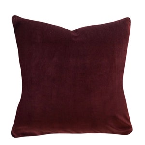May include: A deep burgundy velvet pillow with a square shape and a smooth, soft texture.